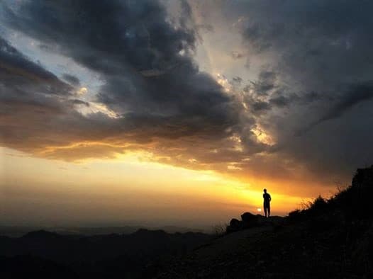 Cinematic golden sunset horizon overlooking endless mountain valleys with a lone wanderer